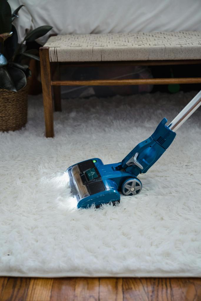 A small vacuum vacuums a white furry rug.